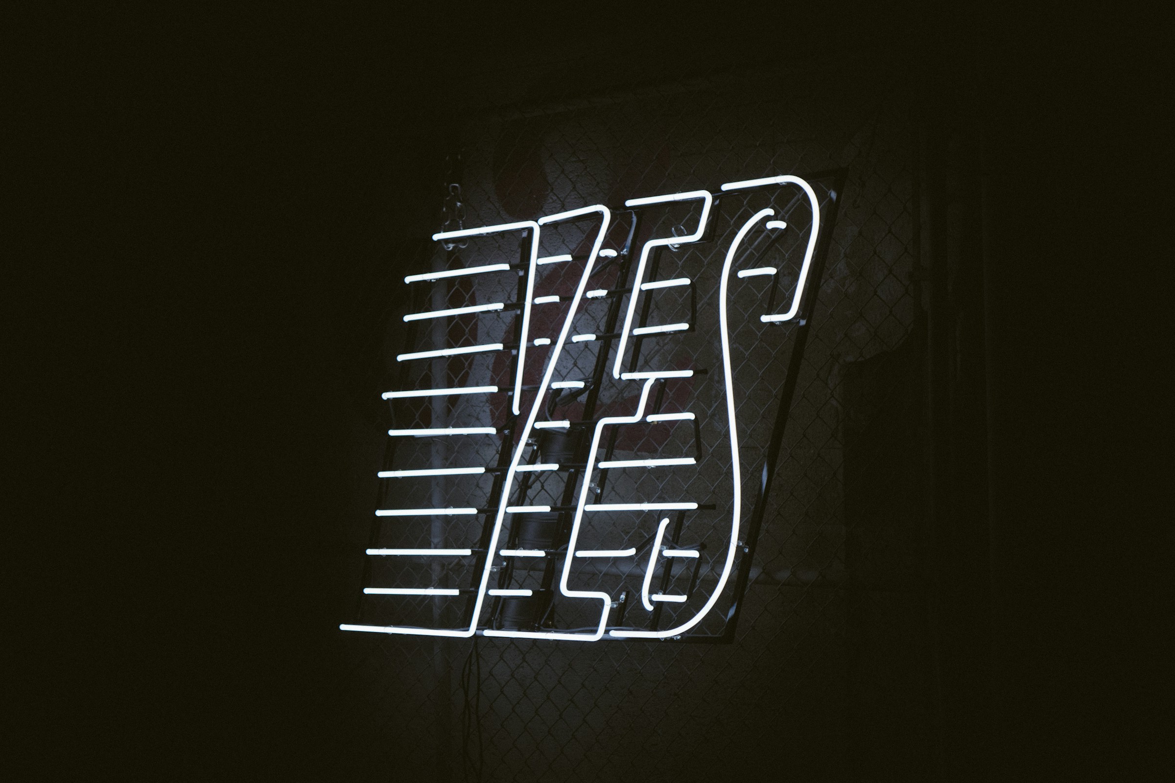 Ein Bild mit einem schwarzen Hintergrund, auf dem in leuchtenden weißen Neonbuchstaben das Wort "Yes" strahlt. Ja zu Einwandbehandlung im Vertrieb.